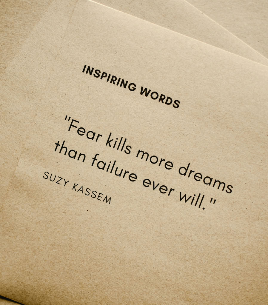 Motivational quote 'Fear kills more dreams than failure ever will.' by Suzy Kassem on paper texture.