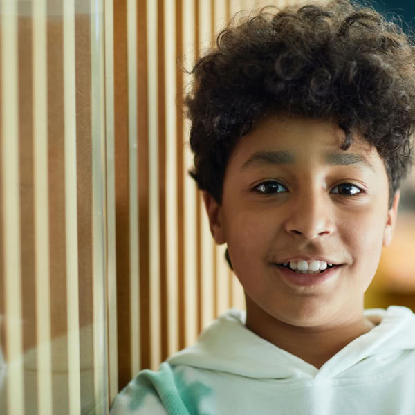 Close-up portrait of a young boy smiling warmly indoors with a blurred background.